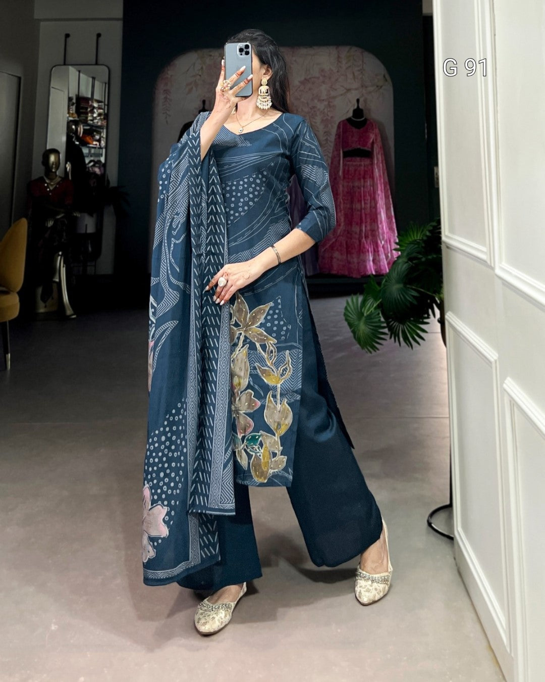 Woman in a blue traditional outfit with floral patterns taking a mirror selfie.