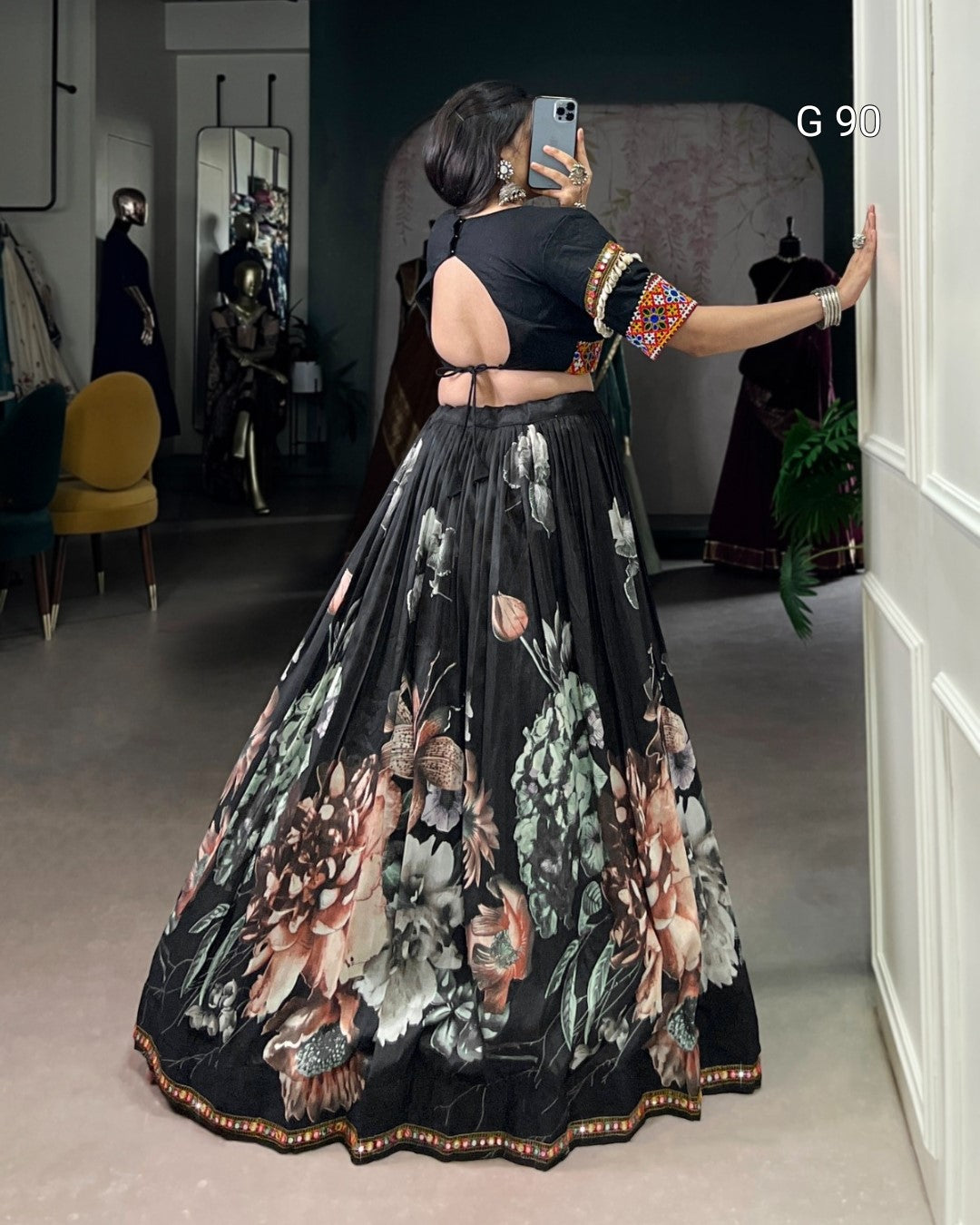 Woman taking a mirror selfie wearing a black floral lehenga in a room.