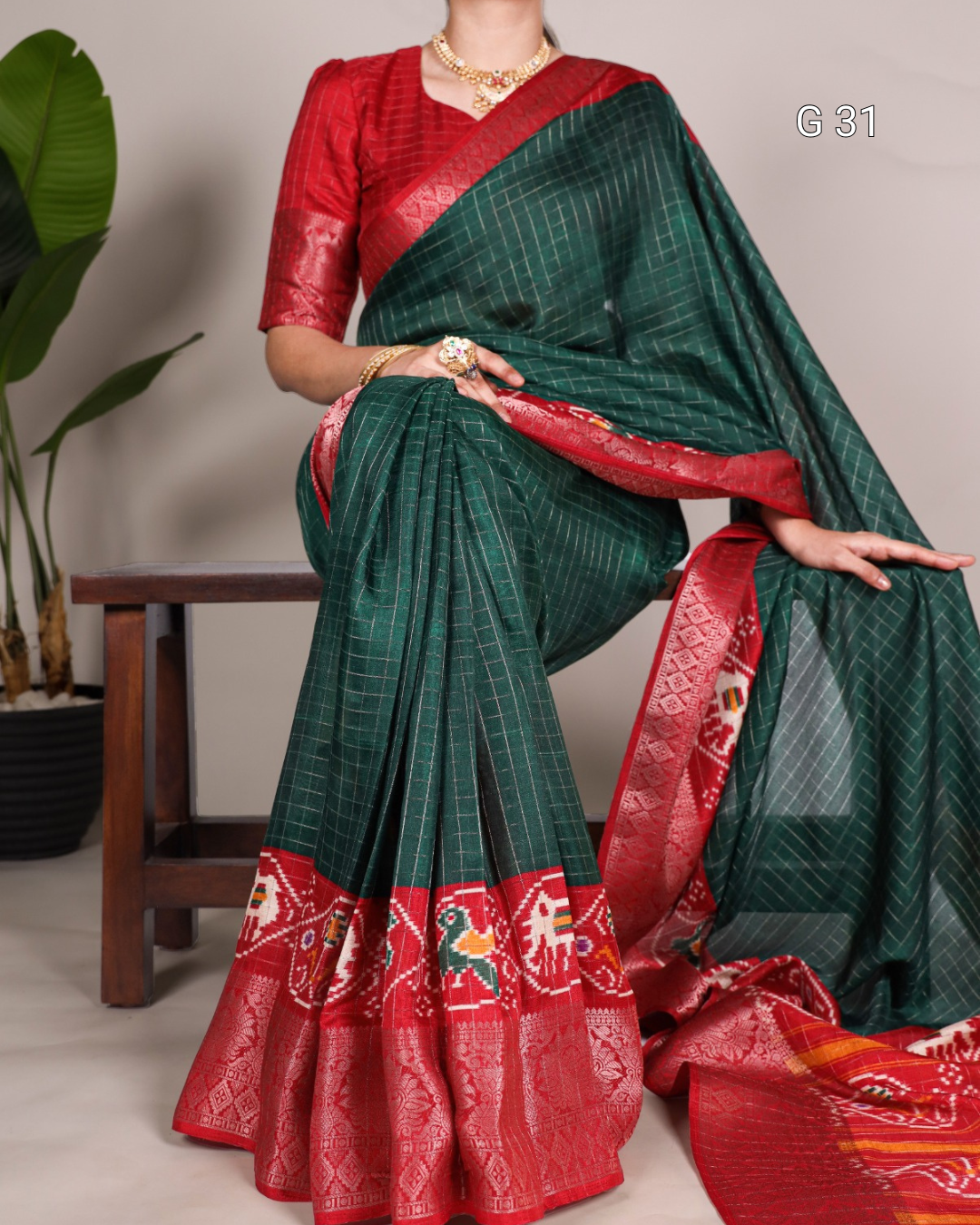Green and red saree with intricate patterns, displayed by a person against a neutral background.