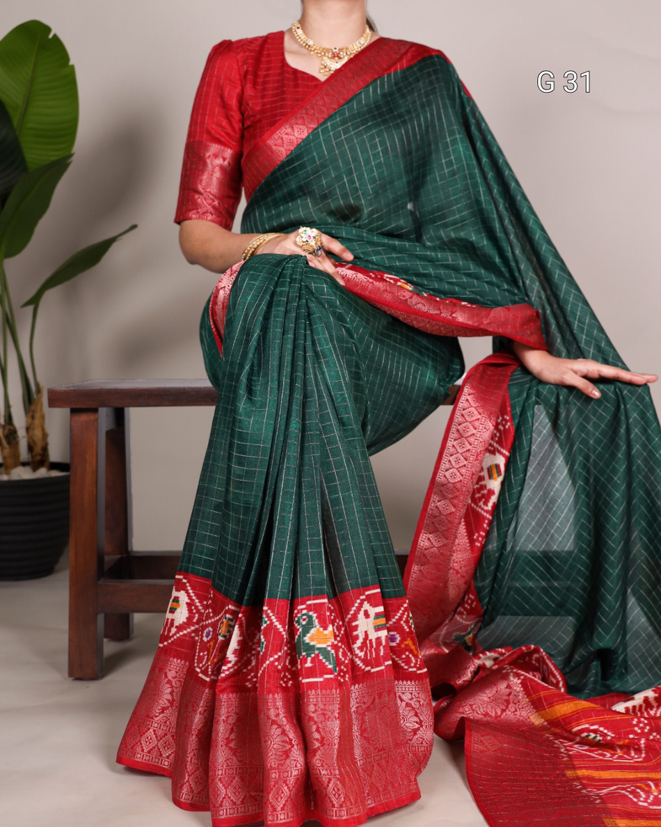 Green and red saree with intricate patterns, displayed by a person against a neutral background.