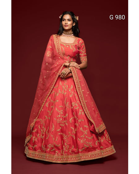 A woman modeling a traditional red lehenga choli set with intricate gold embroidery, set against a solid dark red background. The set includes a red flared skirt (lehenga), a matching embroidered blouse (choli), and a sheer red dupatta with gold borders.