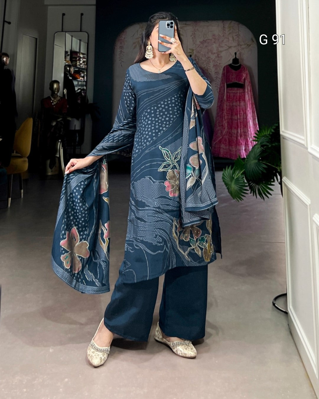 Woman wearing a blue floral outfit taking a mirror selfie in a room.