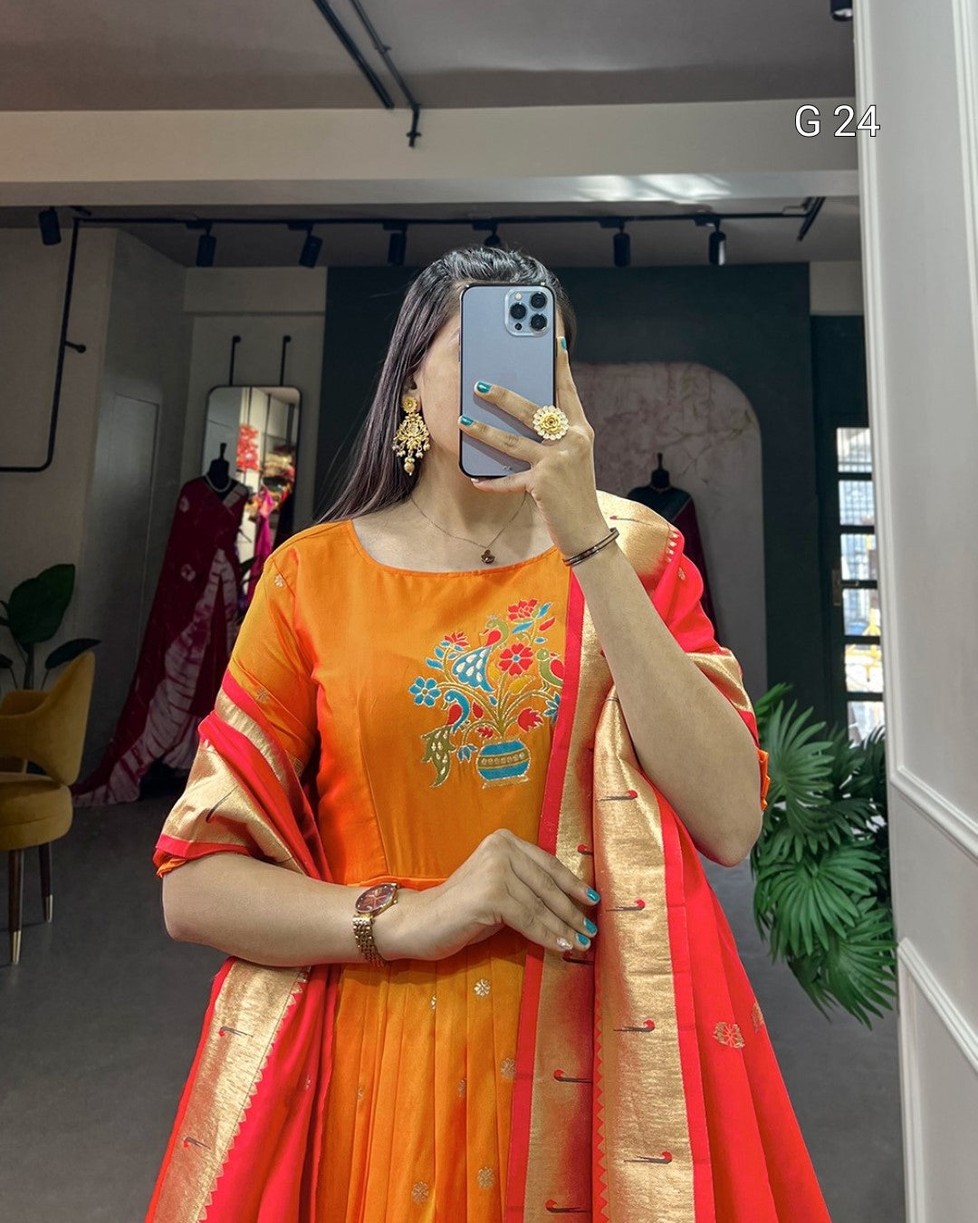 Person wearing an orange and red traditional outfit with floral patterns indoors.