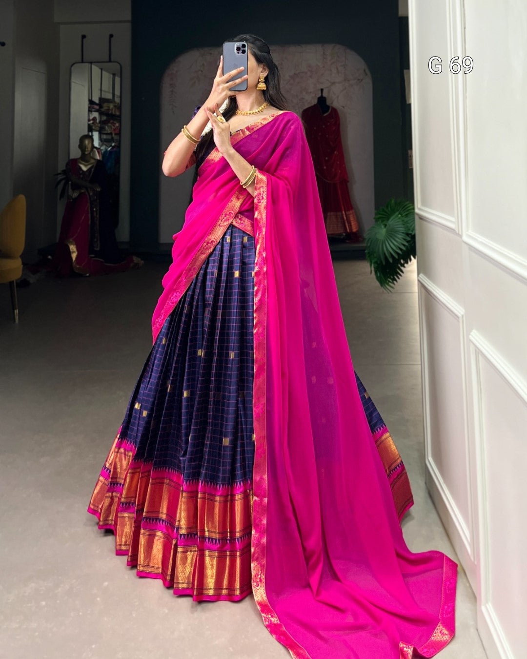 Person wearing a bright pink saree with a blue and red patterned skirt, standing indoors.