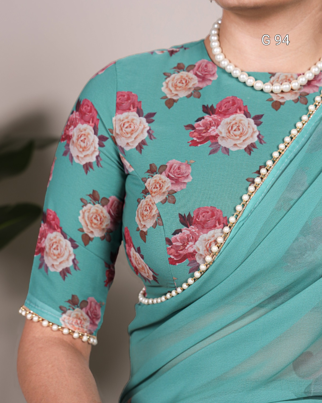 Teal saree with floral patterns and pearl border on a neutral background