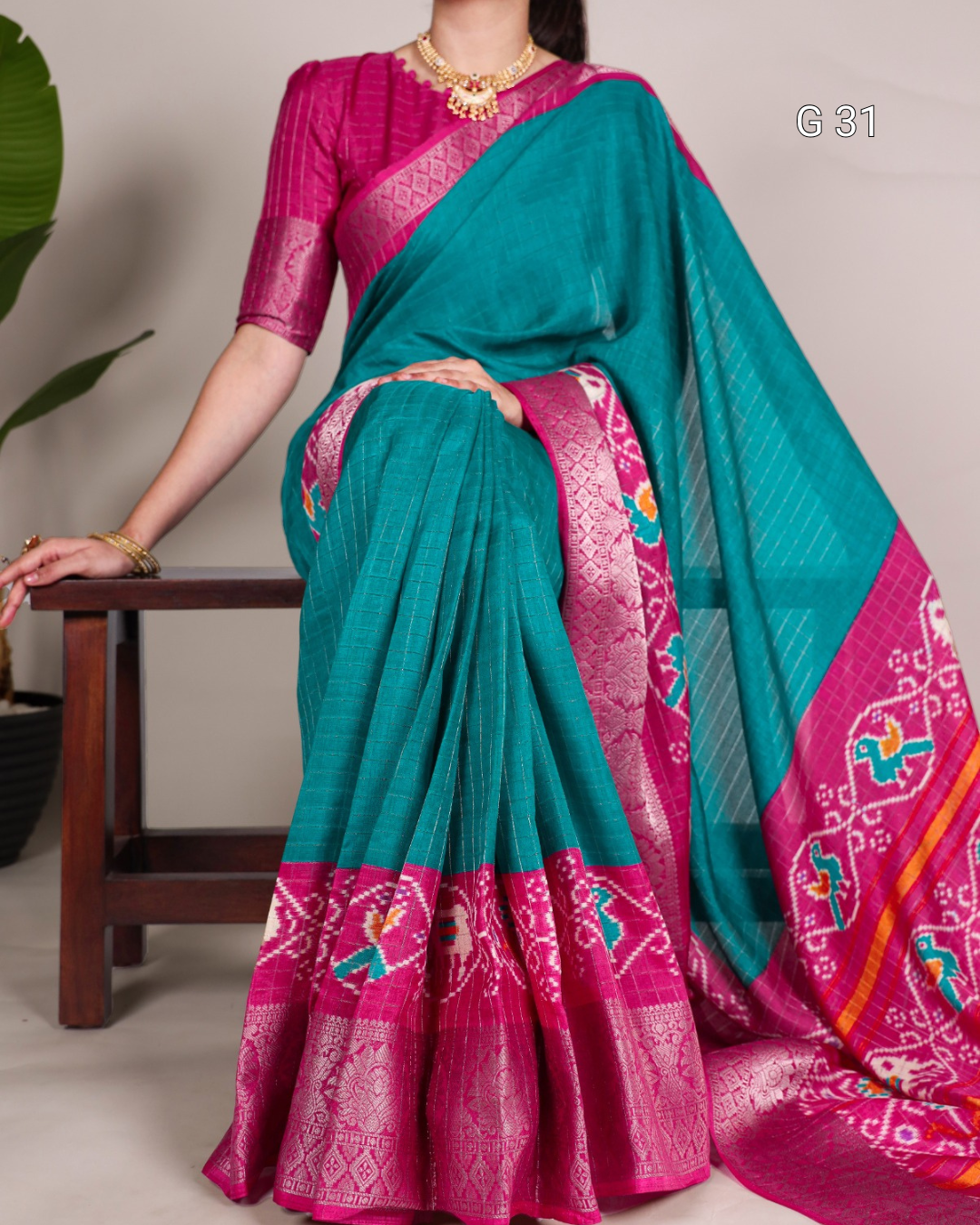 Teal and pink saree with a patterned border, worn by a person, on a neutral background.