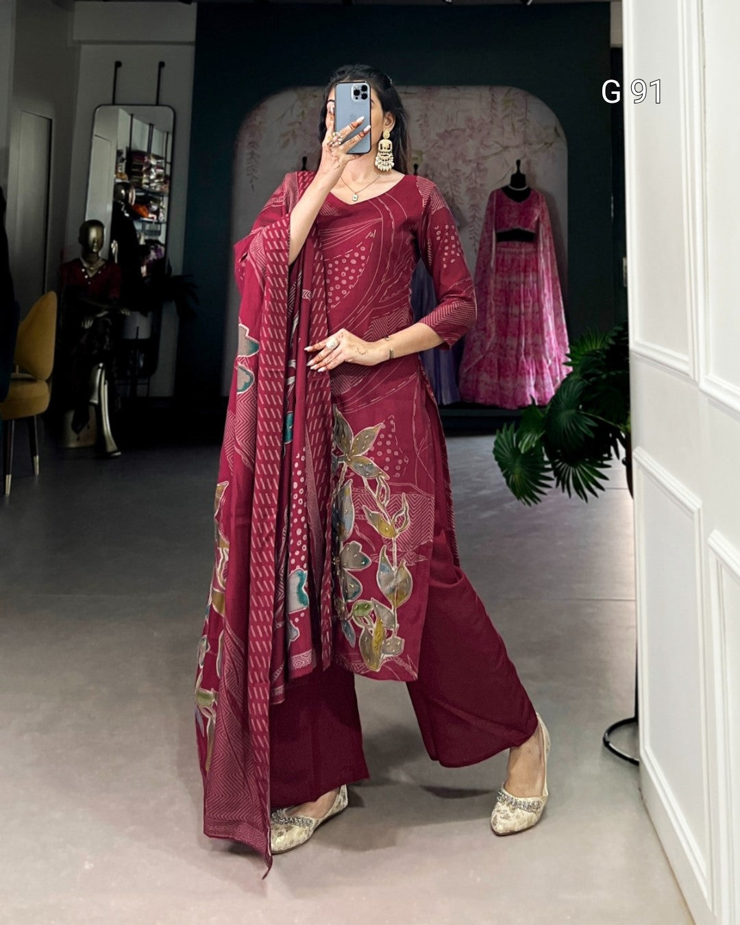 Woman in a maroon traditional outfit with floral patterns in a room.