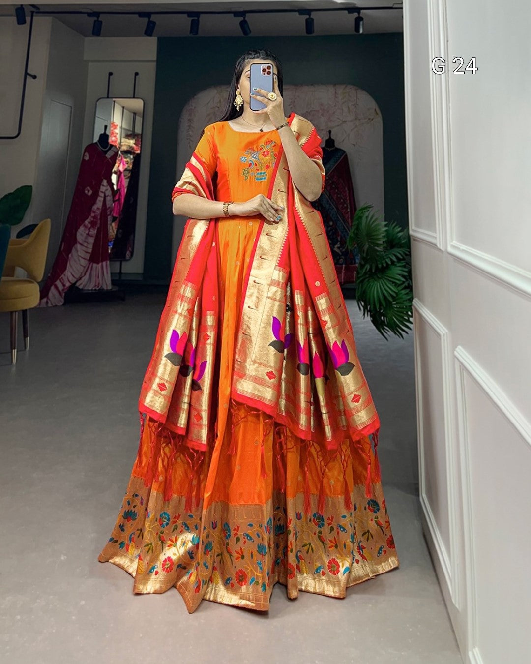 Person wearing an orange and gold traditional outfit with floral patterns in a room.