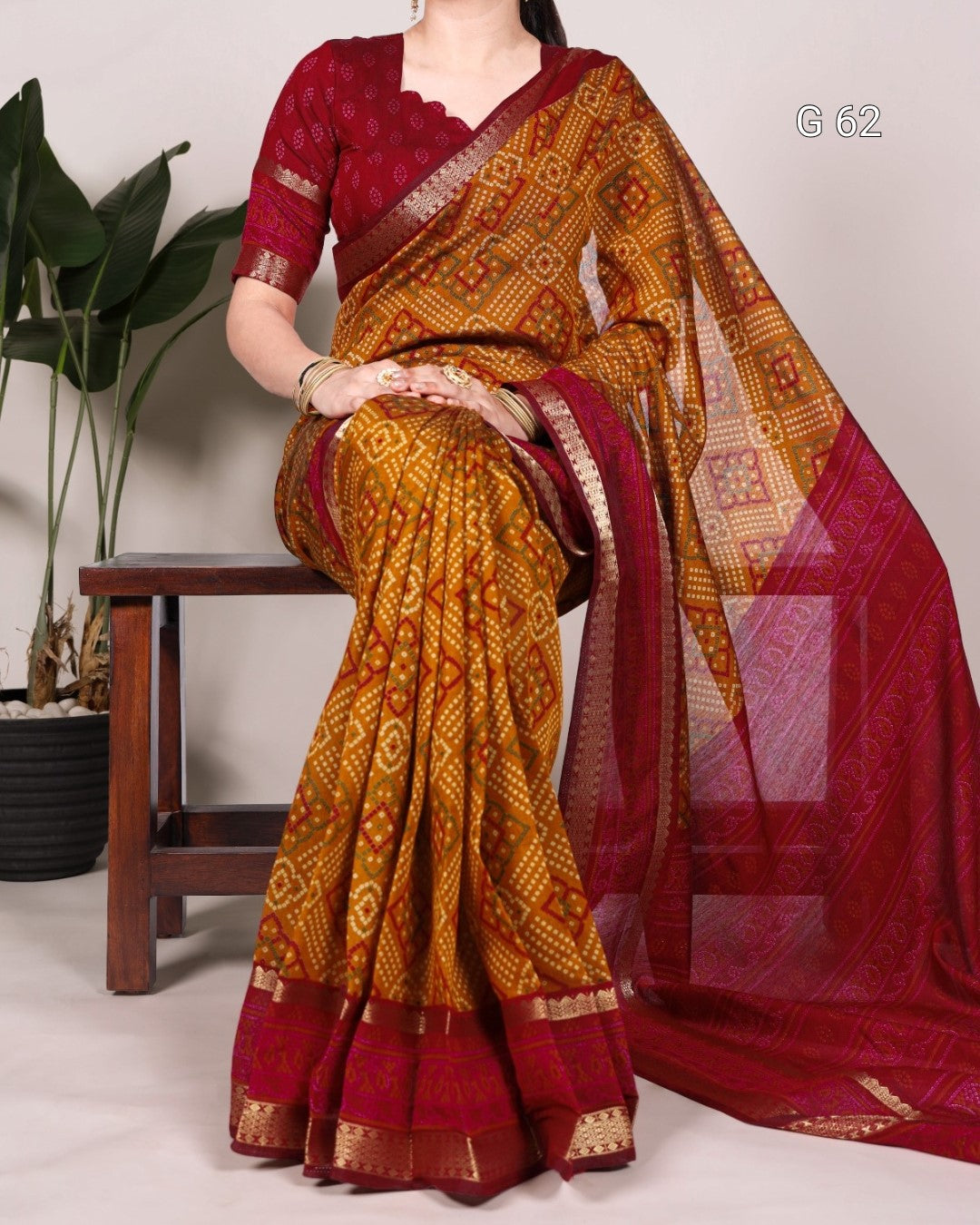 Woman wearing a traditional saree with a red and gold pattern, sitting on a wooden stool.