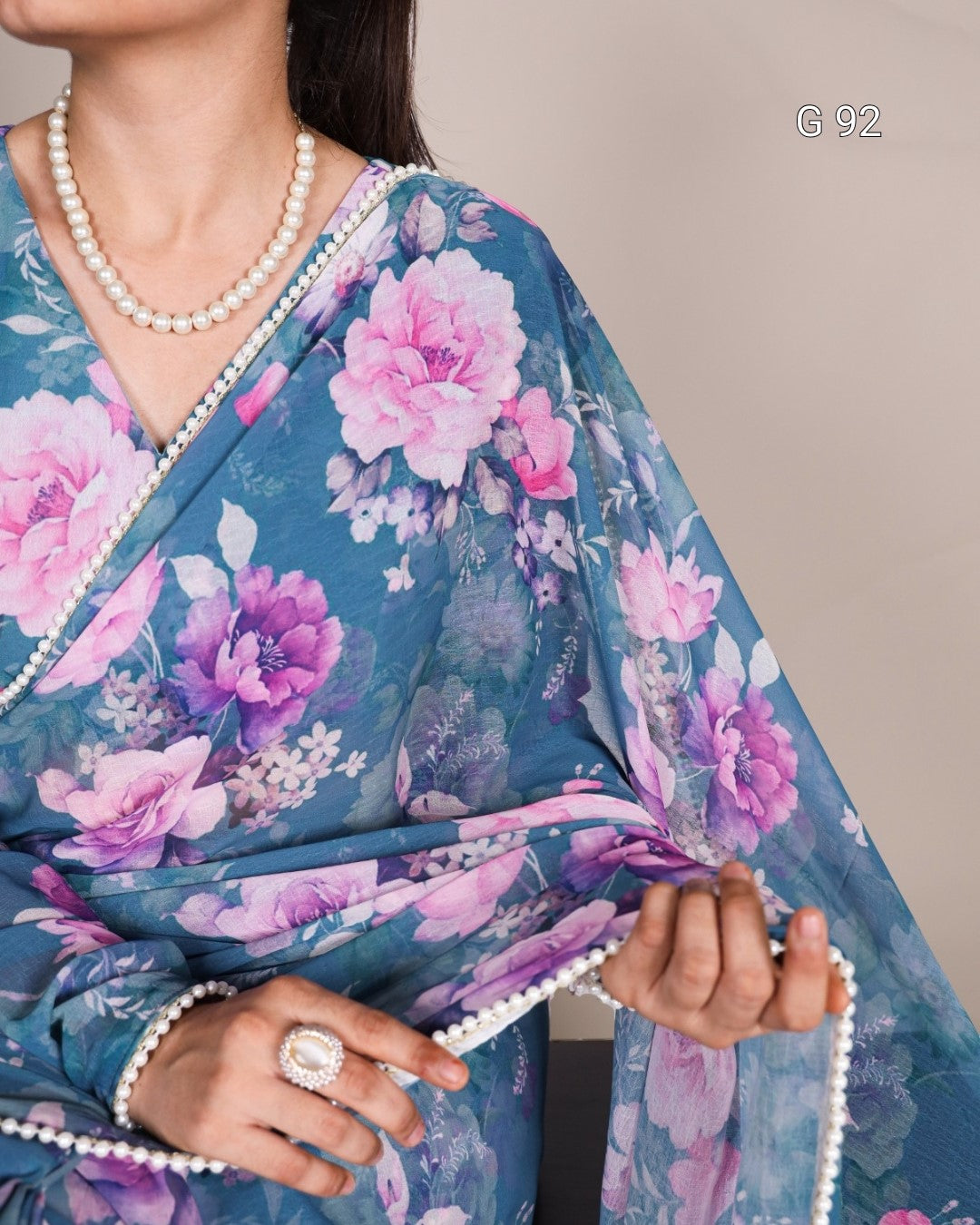 Woman wearing a blue floral saree with pink and purple flowers, holding it with both hands.