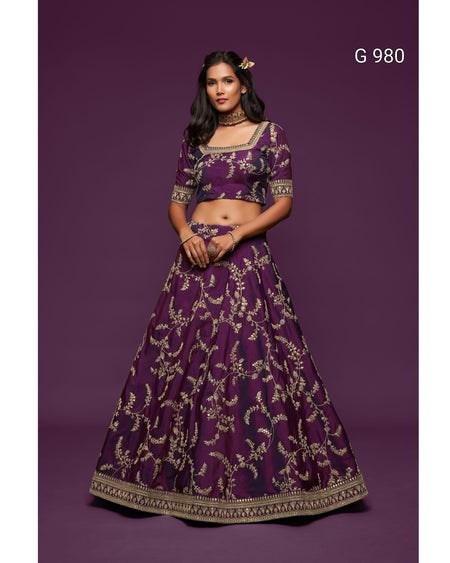 A woman modeling a deep purple lehenga choli set with intricate gold embroidery, set against a solid dark purple studio background. The text 'G 980' is visible in the top right corner.