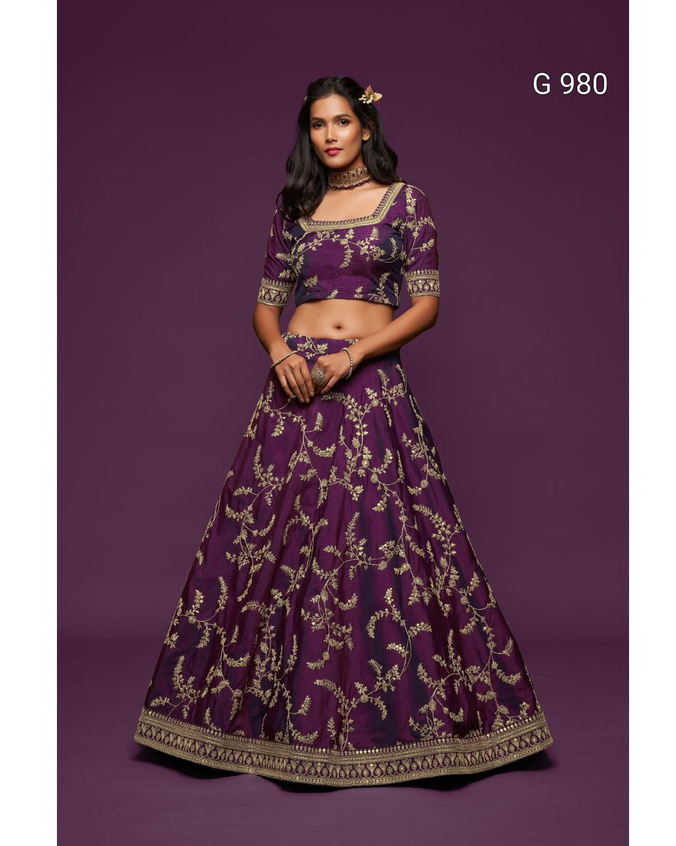 A woman modeling a deep purple lehenga choli set with intricate gold embroidery, set against a solid dark purple studio background. The text 'G 980' is visible in the top right corner.