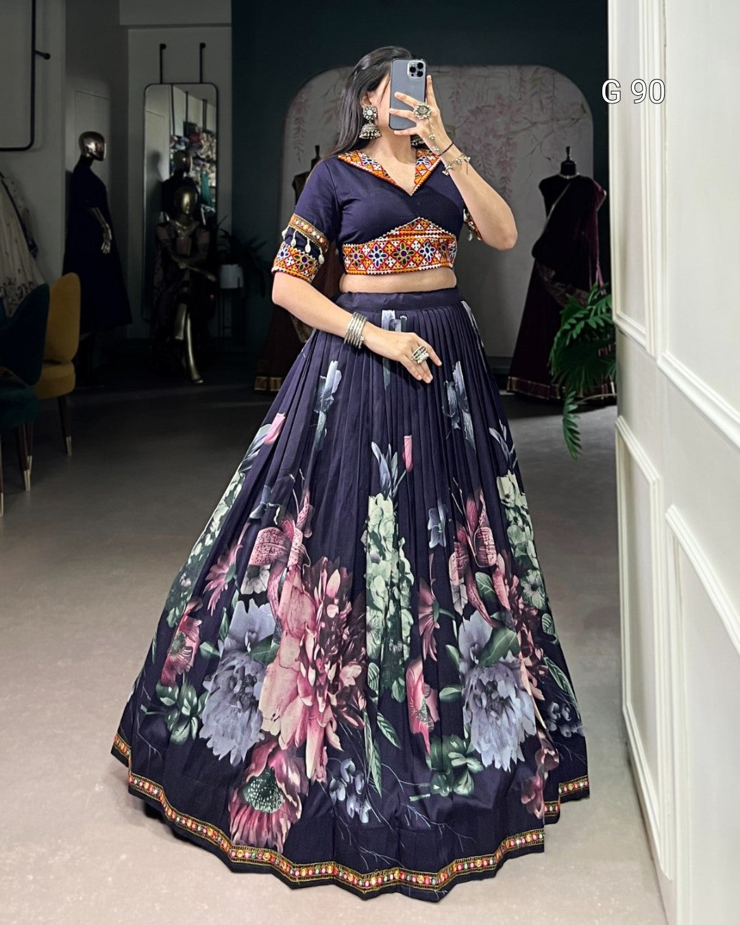 Woman wearing a dark blue floral lehenga in a room with mirrors and furniture.