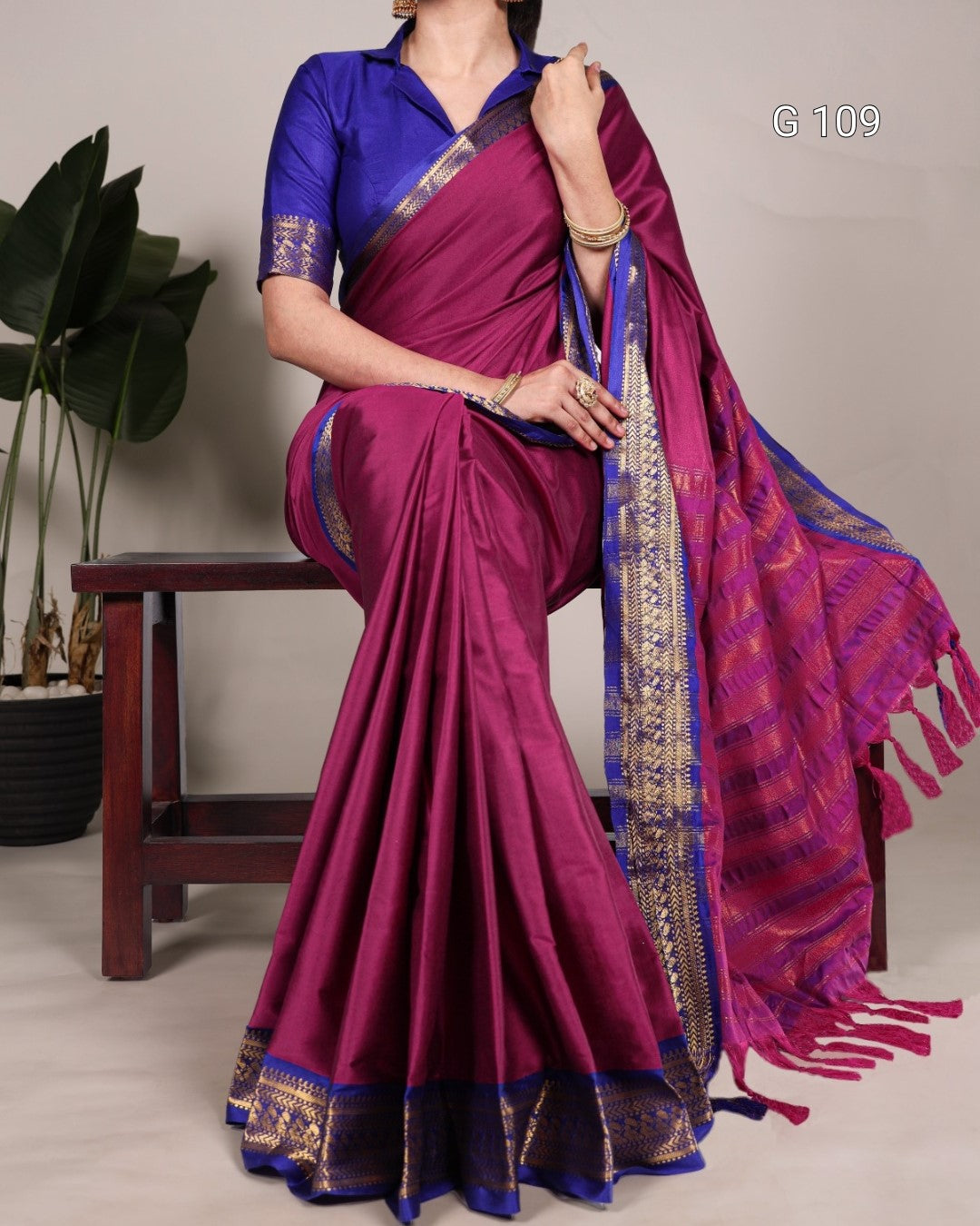Woman wearing a purple saree with a blue blouse, sitting on a chair.