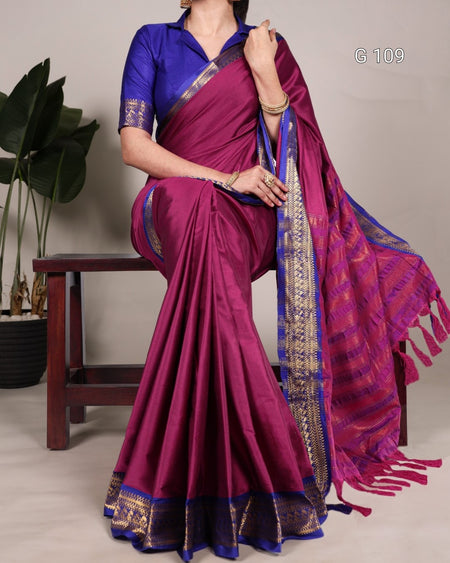 Woman wearing a purple saree with a blue blouse, sitting on a chair.