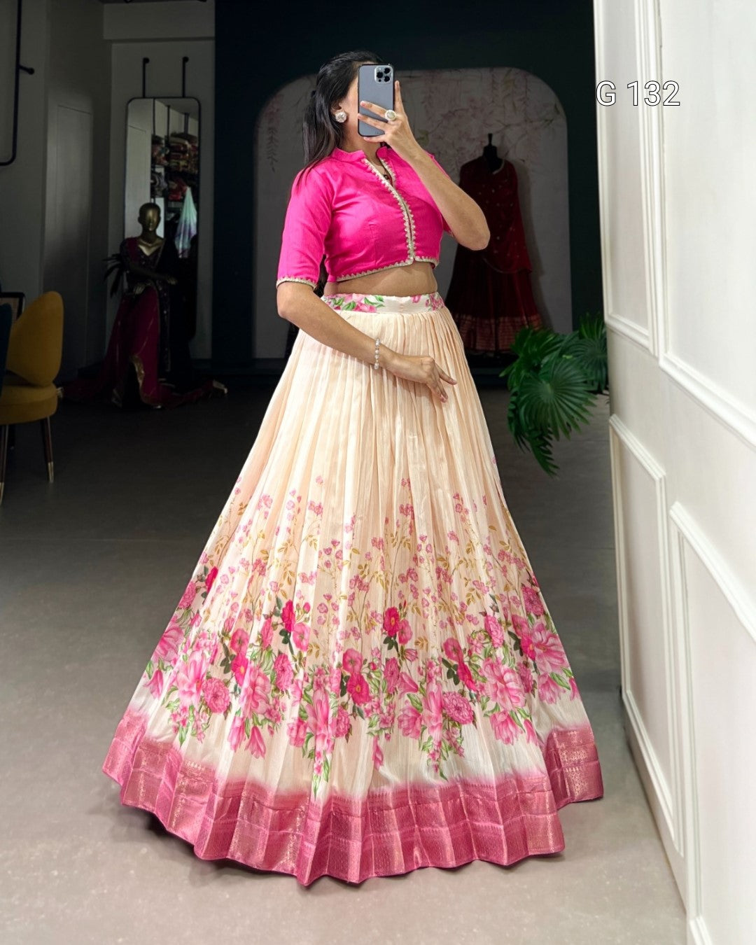Woman wearing a pink blouse and floral skirt in a room with a mirror and plant.
