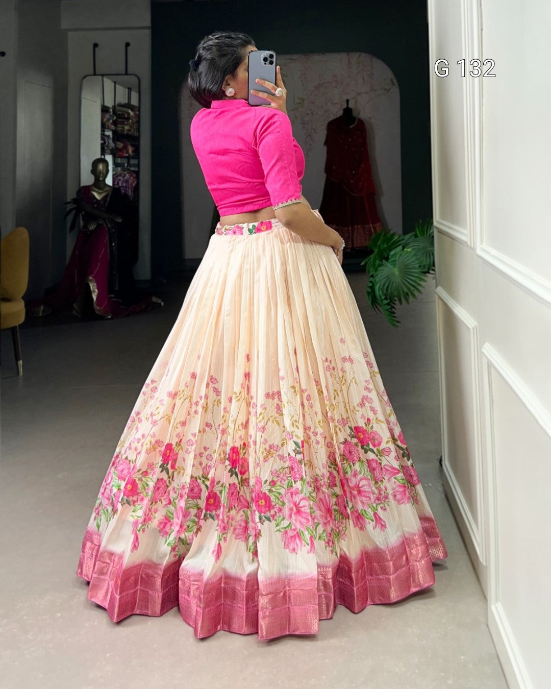 Person wearing a pink blouse and floral skirt in a room with mirrors and a plant.