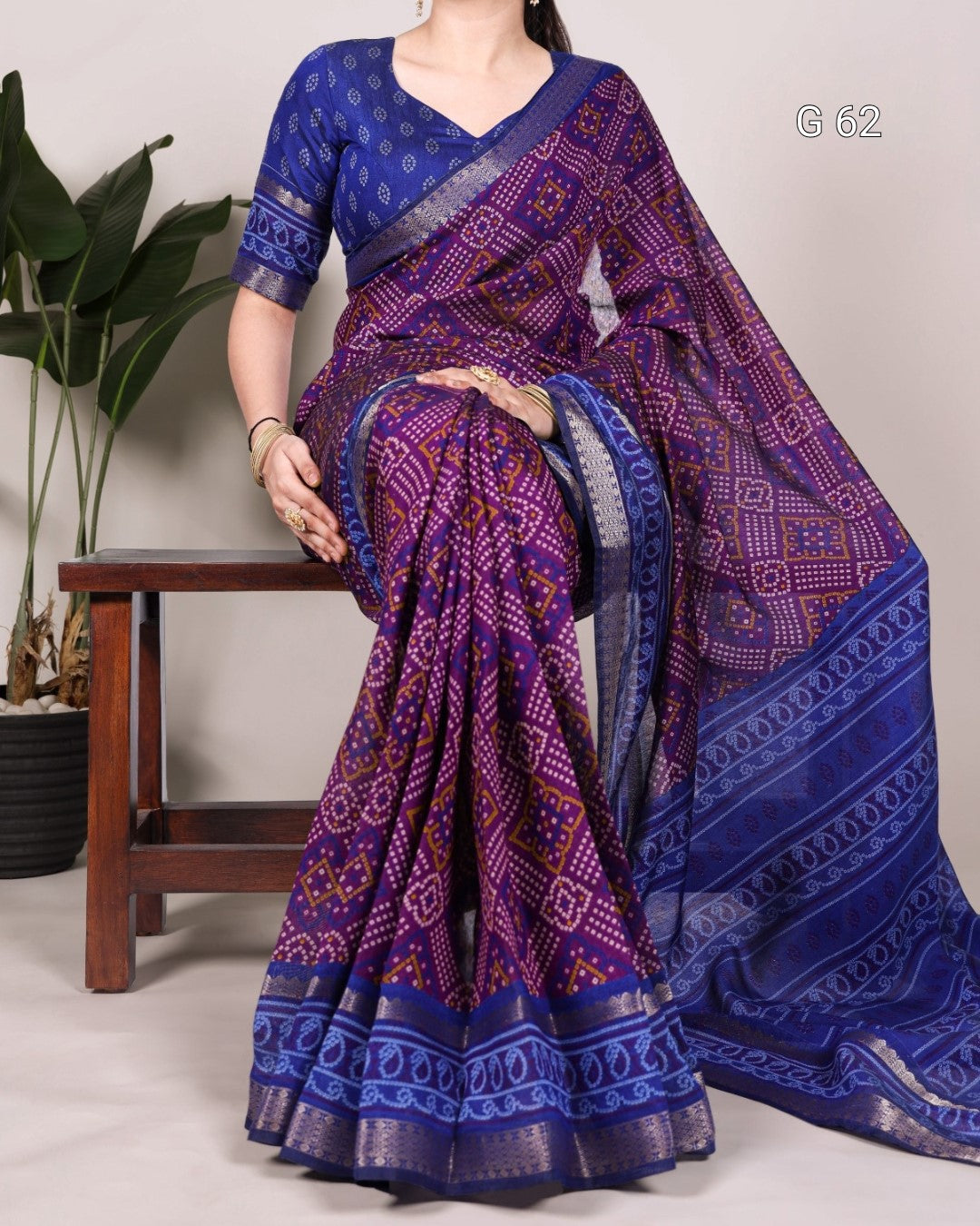 Woman wearing a blue and purple saree with a plant and wooden stool in the background