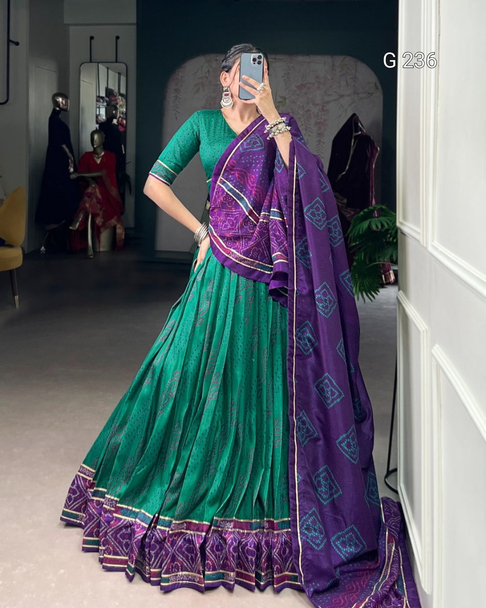 Woman wearing a green and purple saree in a room with mirrors and furniture.