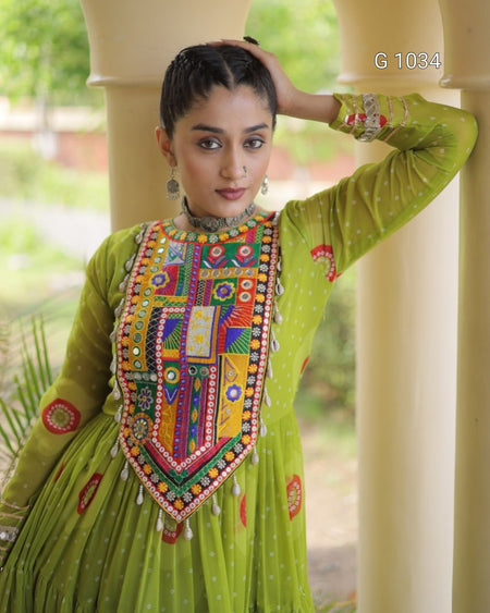 A woman wearing a bright lime green traditional embroidered dress with a heavily decorated multicolor embroidered chest panel, standing in a covered outdoor walkway with cream pillars.