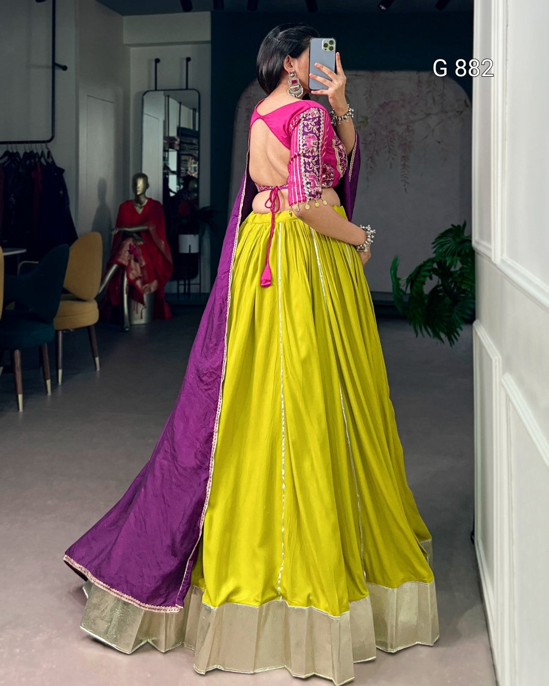 Woman wearing a bright yellow and purple traditional outfit, standing in a room with a mirror and chair.