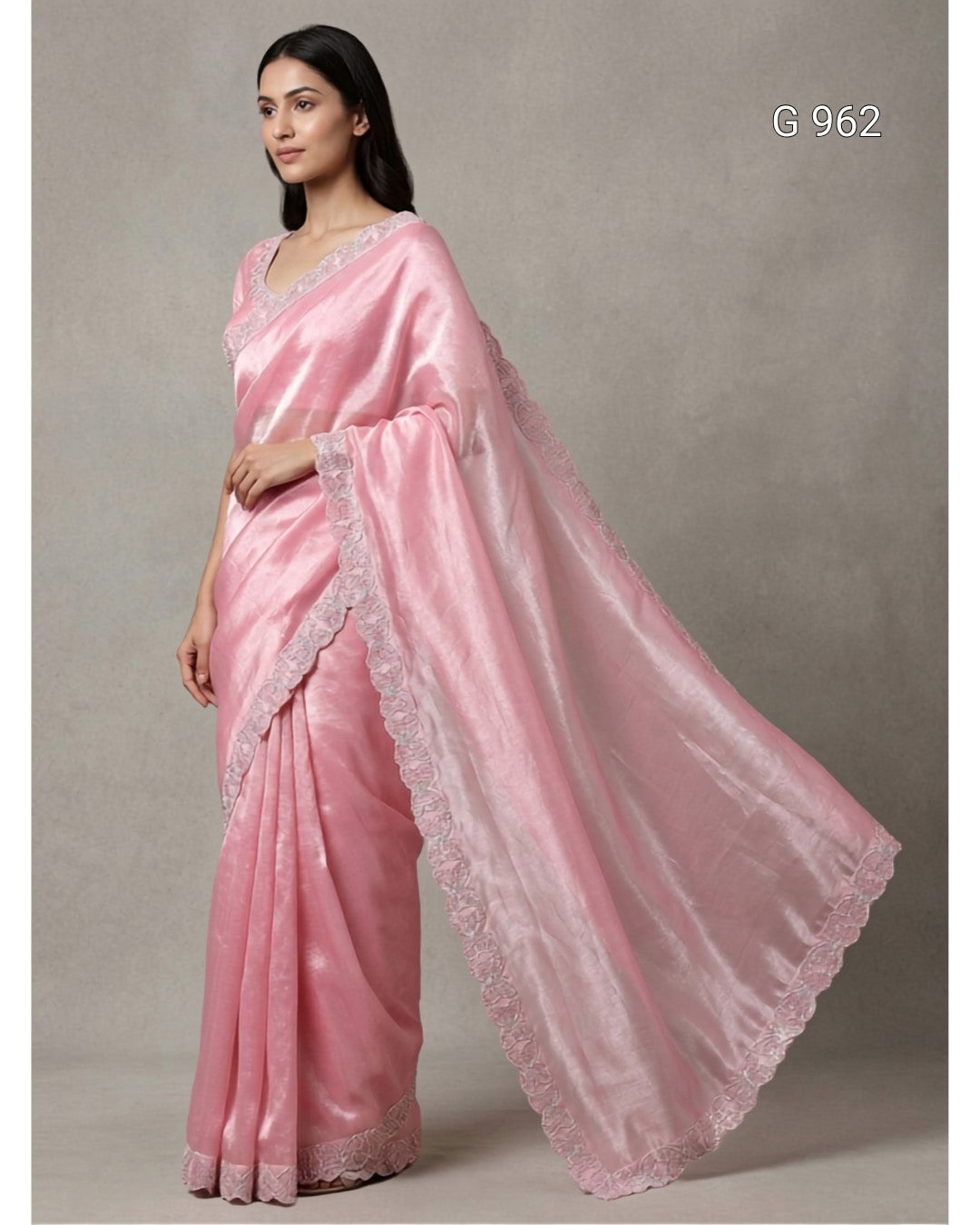 A woman modeling a light pink silk saree with a matching dupatta featuring delicate lace borders, set against a neutral gray studio background.