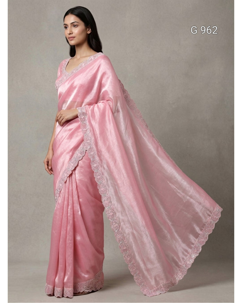 A woman modeling a light pink silk saree with a matching dupatta featuring delicate lace borders, set against a neutral gray studio background.