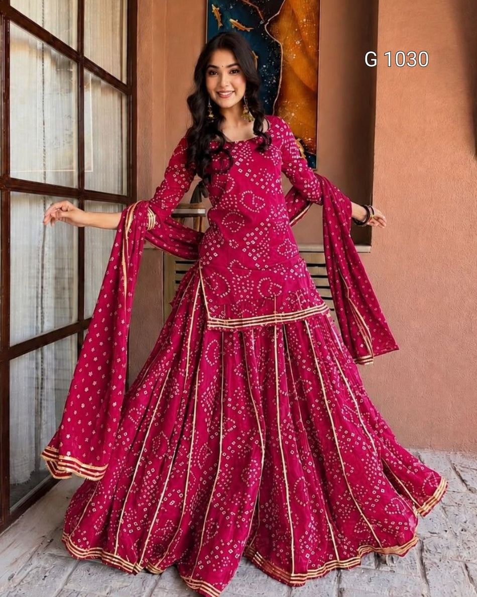 A woman modeling a magenta pink flared traditional outfit with white bandhani print and gold border details, standing in front of a rustic wall and window frame. The text 'G 1030' appears in the top right.