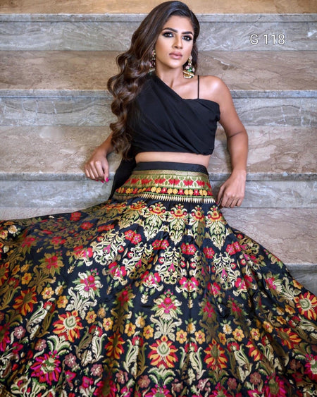 Woman wearing a black top and colorful floral skirt against a stone wall.