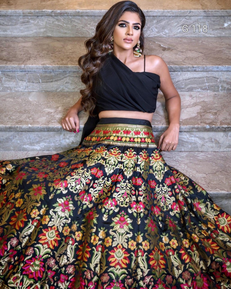Woman wearing a black top and colorful floral skirt against a stone wall.