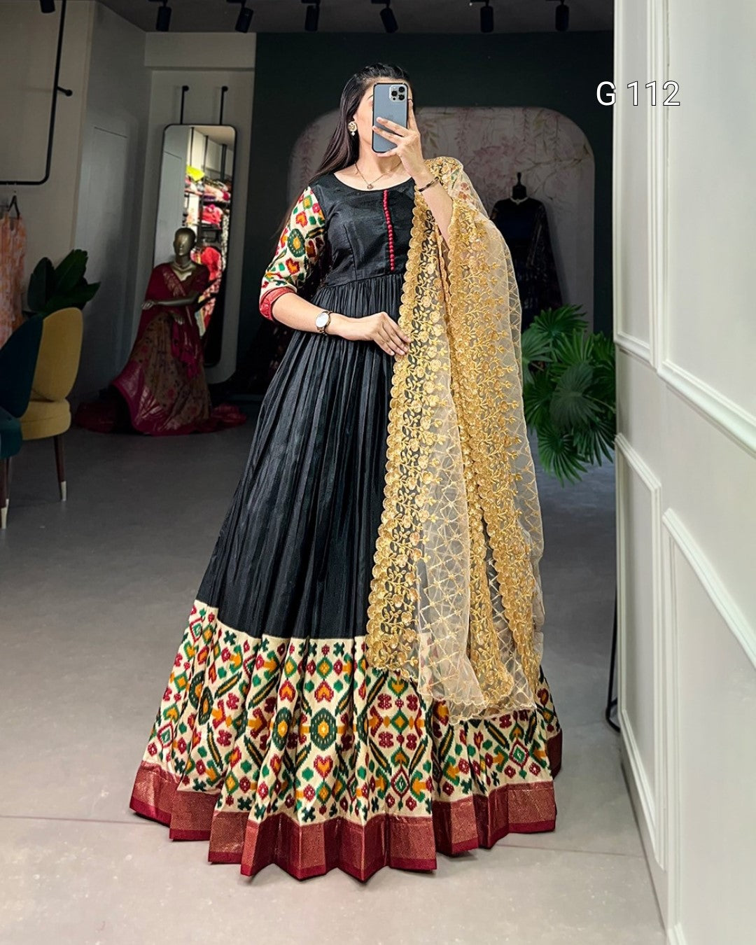 Woman wearing a traditional outfit with a black and patterned skirt, standing in a room.
