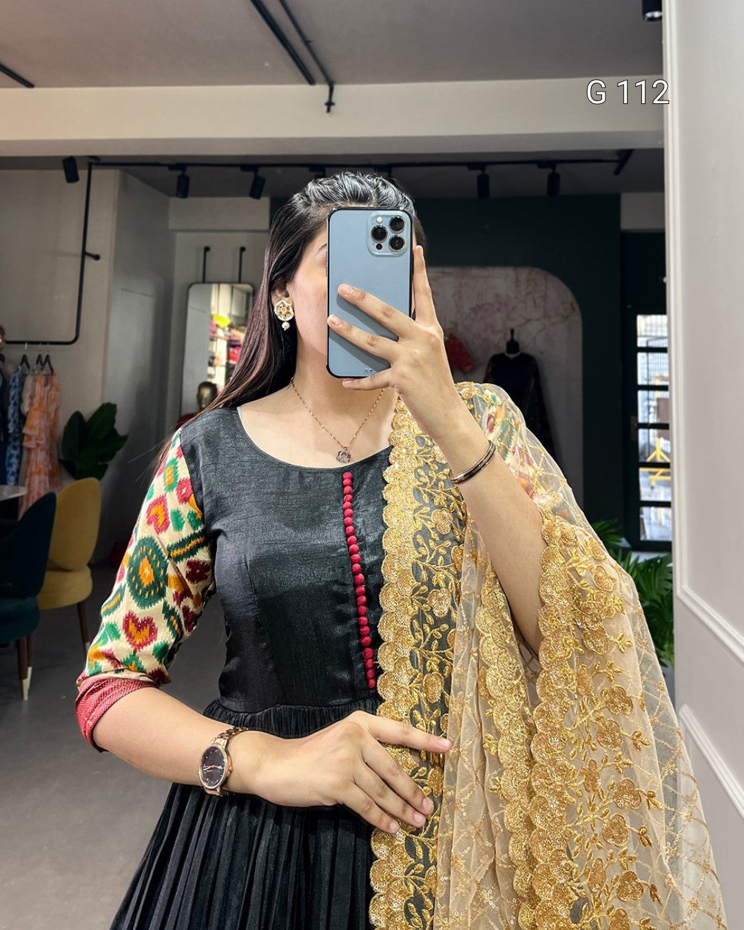 Person wearing a black outfit with colorful sleeves and a gold dupatta, taking a mirror selfie.