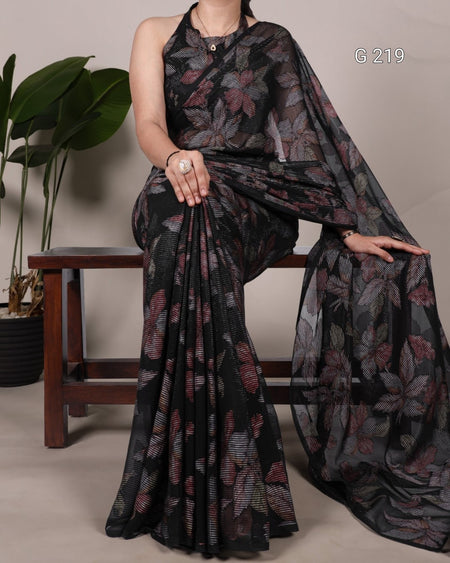 Woman wearing a black floral saree with a plant and wooden stool in the background