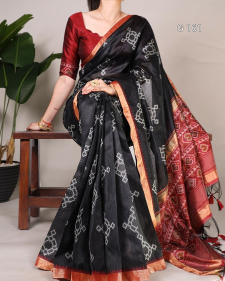 Woman wearing a black saree with red blouse, sitting on a wooden stool.