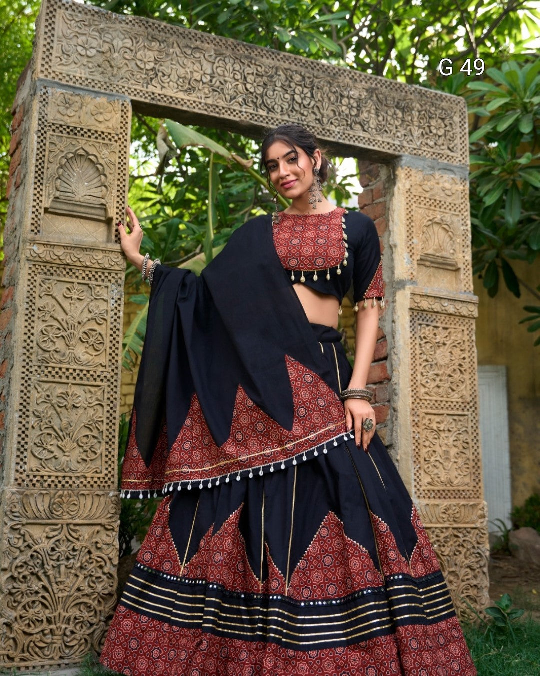Woman in traditional attire standing in front of an ornate stone archway.