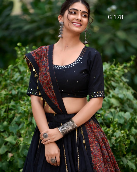 Woman wearing a traditional outfit with a dark blouse and patterned dupatta against a green leafy background.