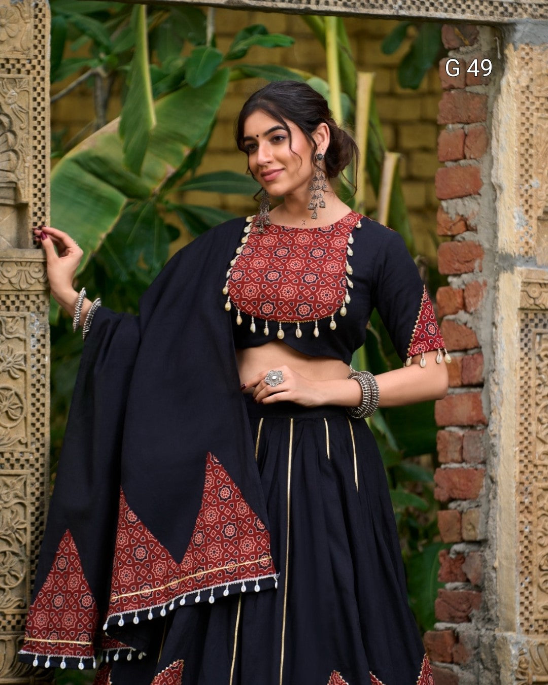 Woman in traditional outfit with red and black patterns against a rustic background