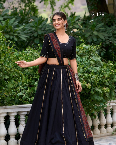 Woman in a black traditional outfit with intricate designs standing outdoors.