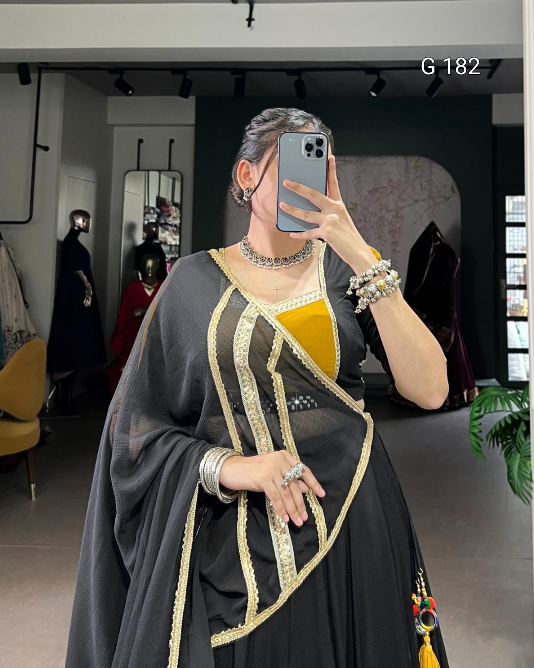 Person wearing a black and gold traditional outfit with jewelry in a room setting.