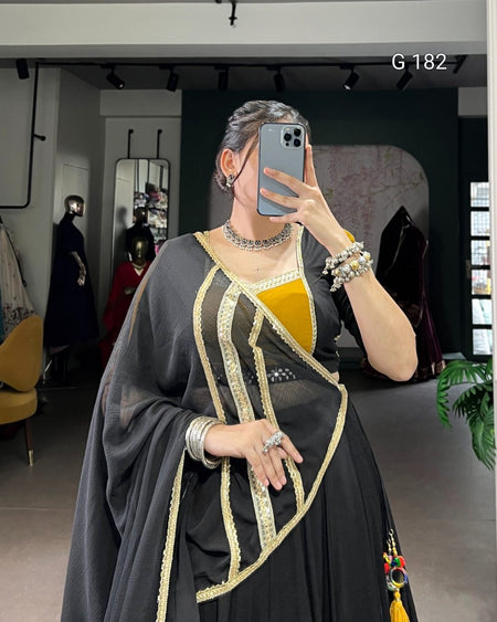 Person wearing a black and gold traditional outfit with jewelry in a room setting.