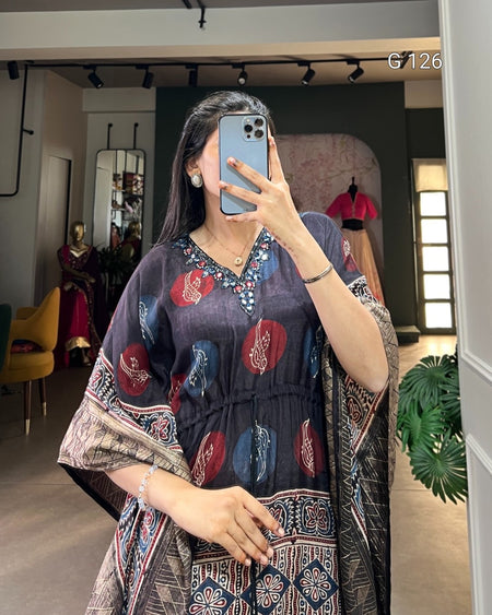 Woman taking a mirror selfie wearing a patterned dress in a room with decor elements.