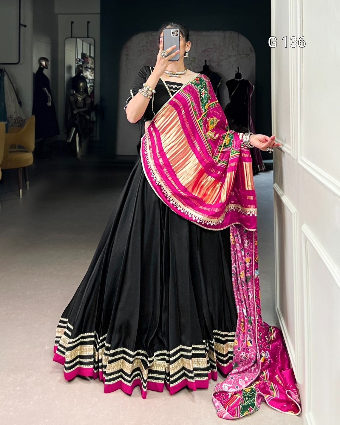 Person wearing a black saree with a colorful border, standing against a white wall.
