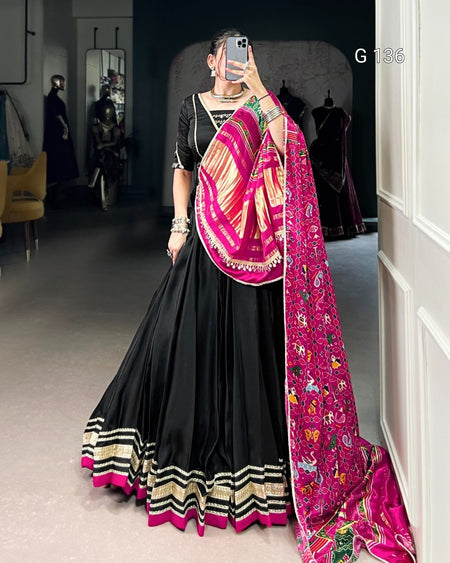 Person wearing a black saree with a pink and gold border, standing in a room.