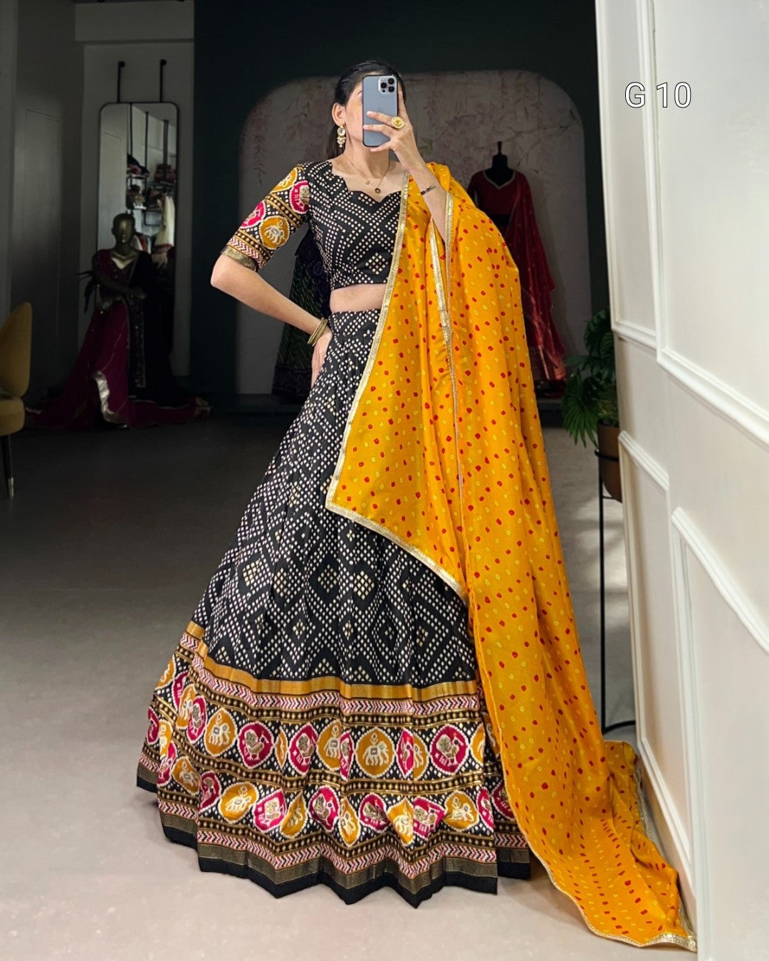 Woman in a traditional black and yellow outfit with a patterned dupatta taking a mirror selfie.