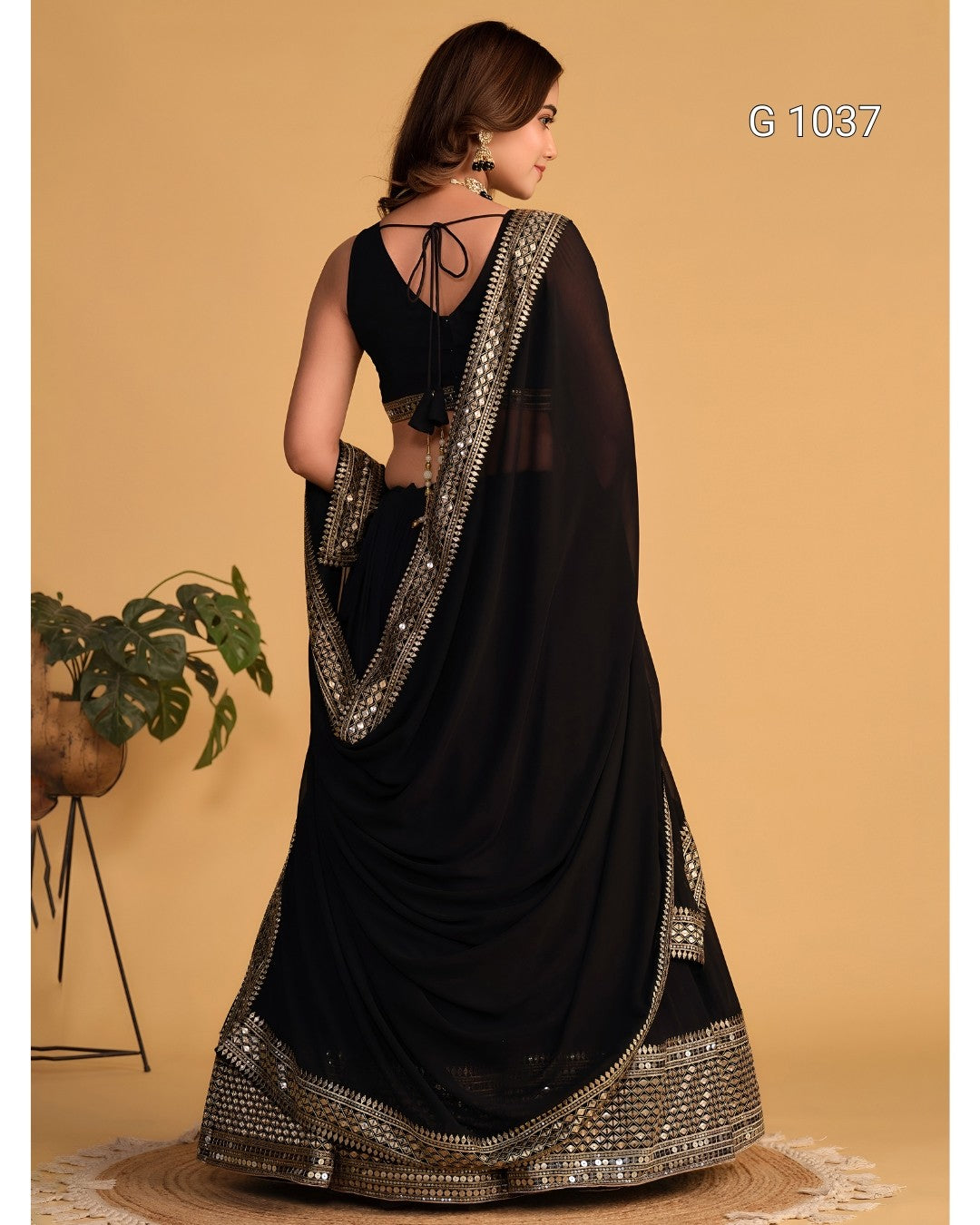 A woman modeling a black georgette saree with heavy silver mirror work borders, shown from the back against a warm beige studio backdrop.
