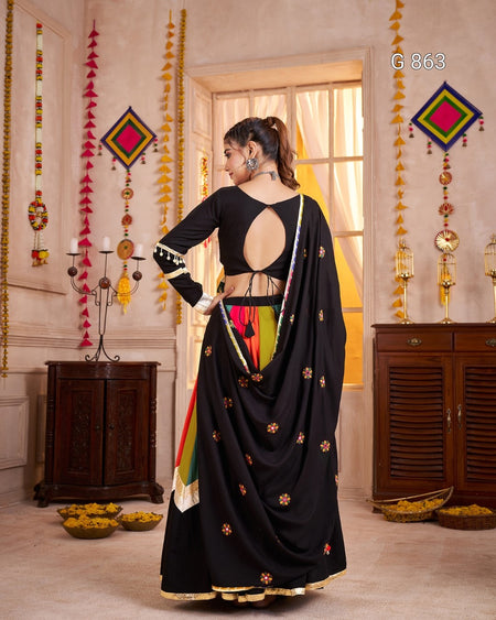 Woman in a black saree with a colorful blouse in a decorated room.