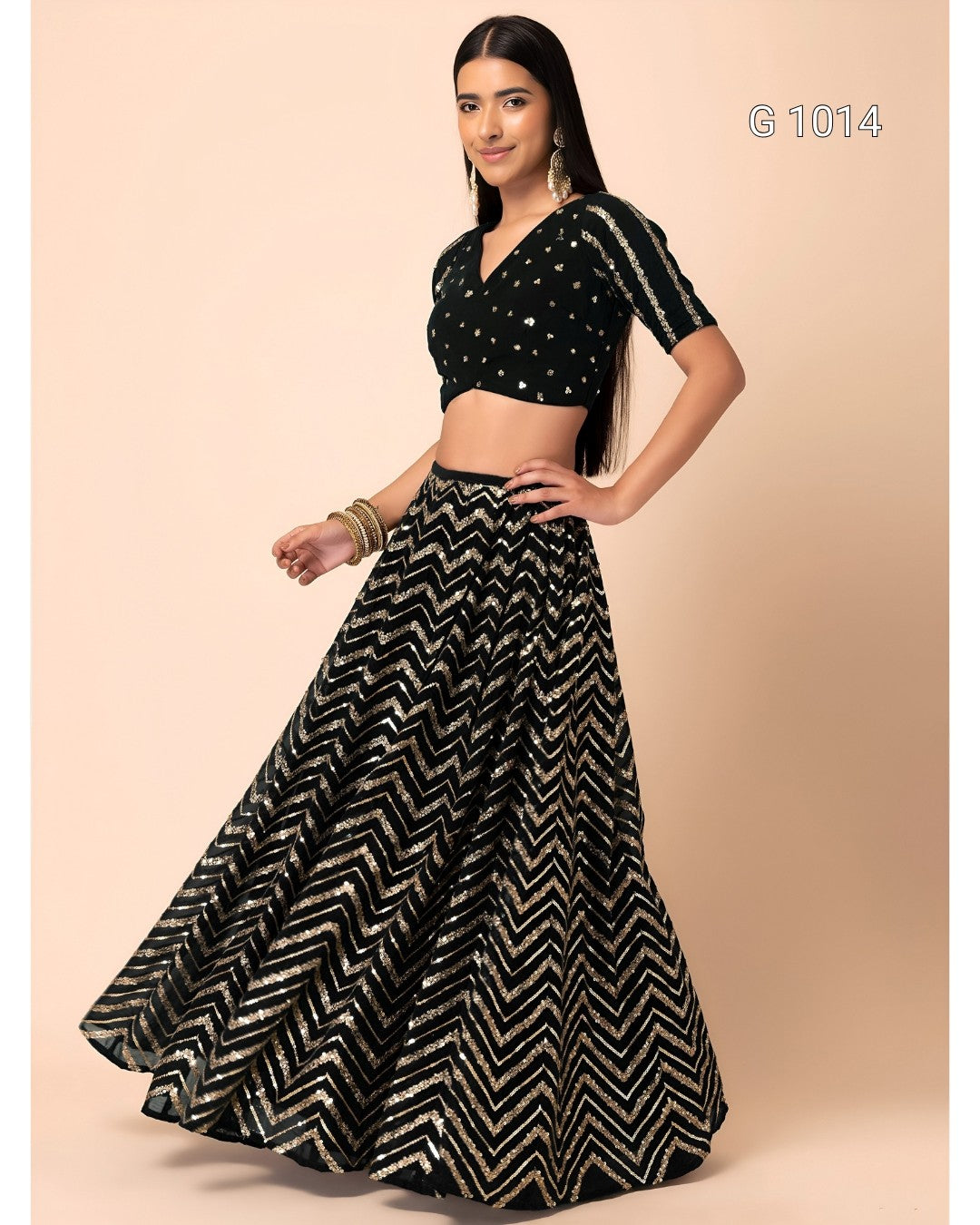 A woman modeling a black and silver chevron-patterned lehenga choli set against a solid beige background. The set features a black crop top with silver embellishments and a matching flared skirt with a silver and black zigzag pattern.