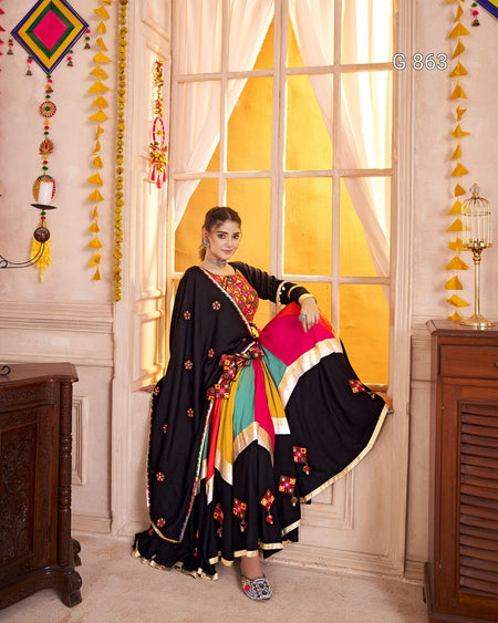 Woman in a colorful saree sitting in a decorated room with yellow curtains and festive decorations.