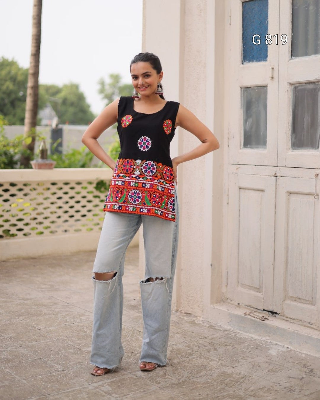 Woman wearing a black top with floral designs and a colorful skirt in an outdoor setting.