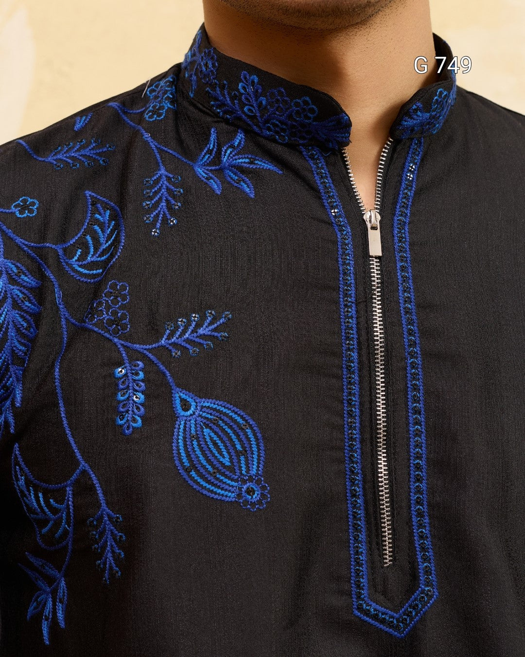Black garment with blue floral embroidery and a zipper on a beige background
